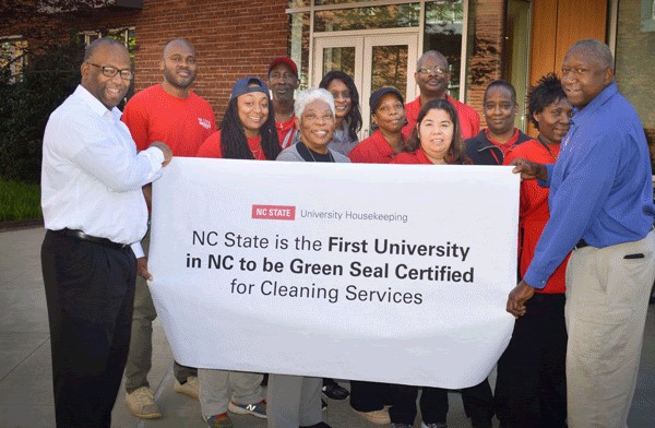 Group of smiling Housekeeping employees holding a banner celebrating that NC State is the First University in NC to be Green Seal Certified for Cleaning Services.
